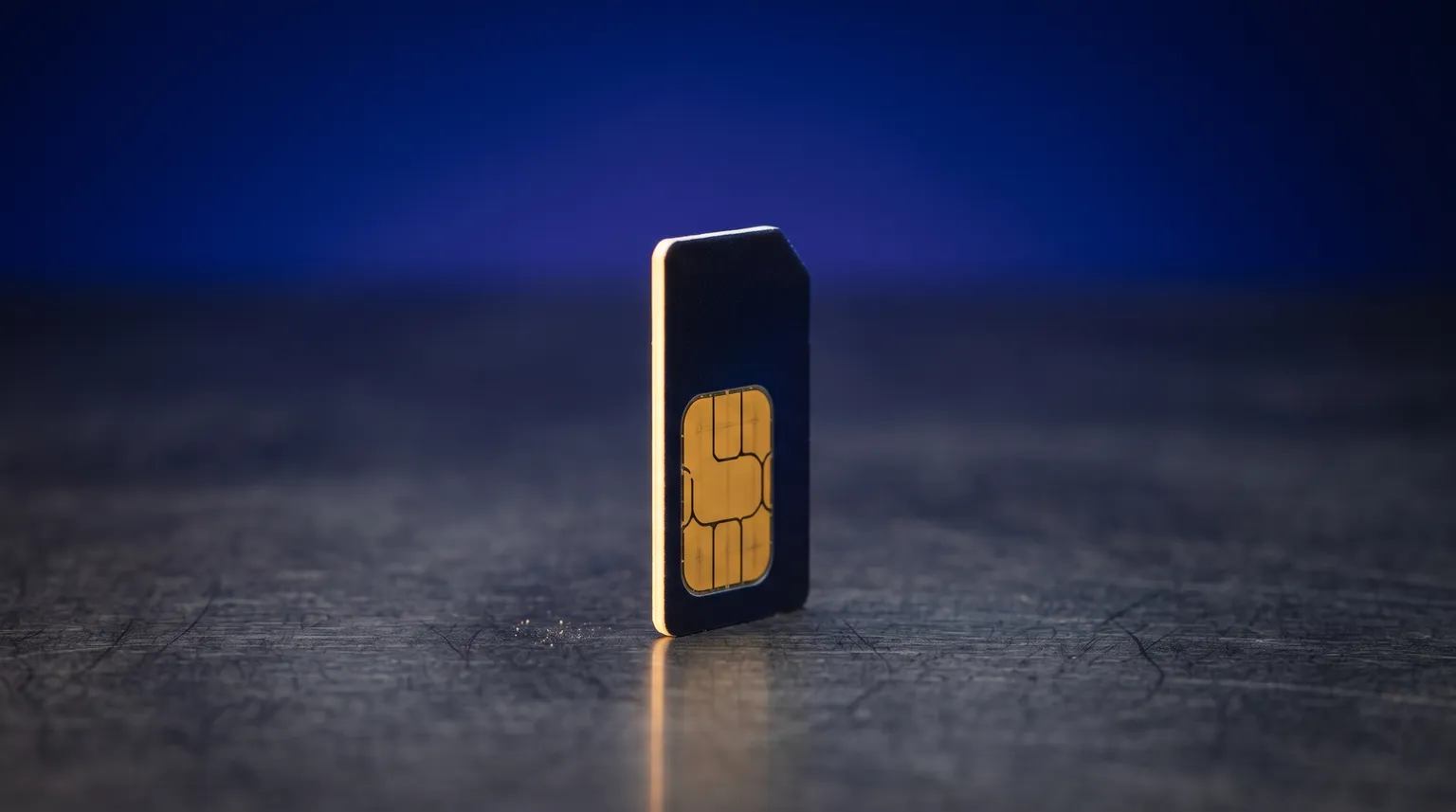 A single SIM card standing on a dark brushed surface, its gold contacts catching the light.