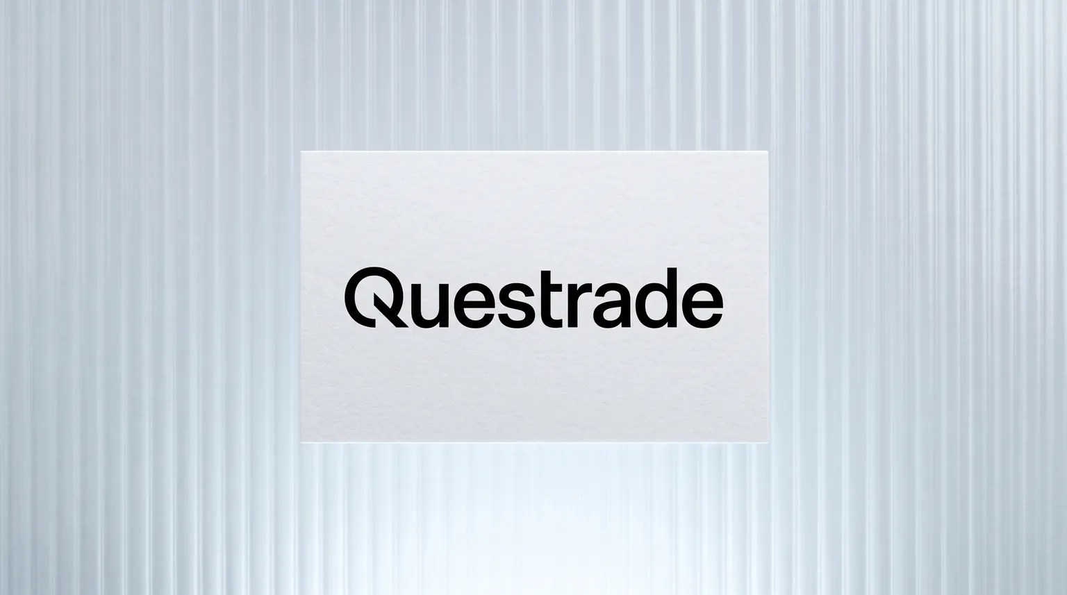 The Questrade logo on a matte white card resting on a pane of ribbed frosted glass.