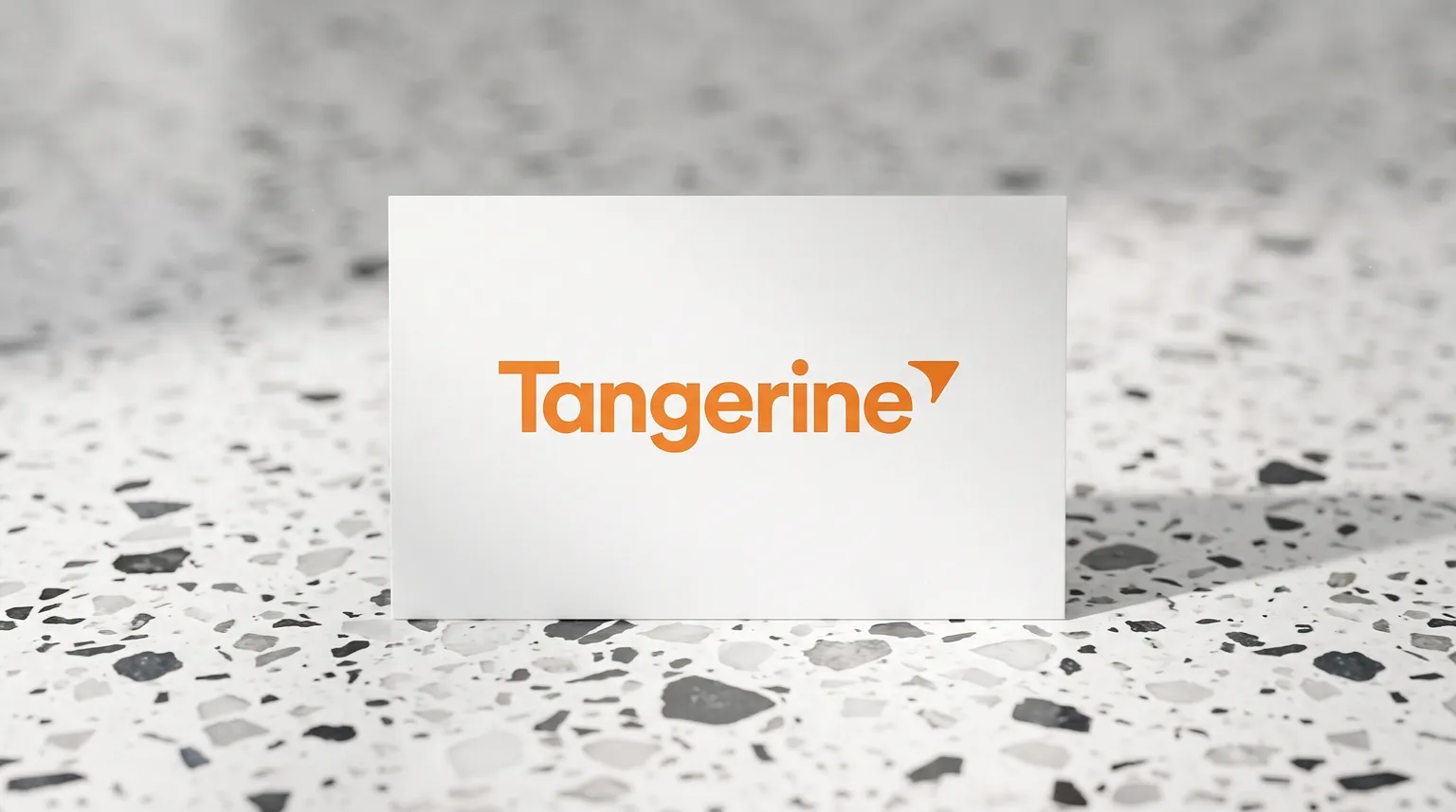 The Tangerine logo on a matte white card standing on a white terrazzo surface flecked with charcoal, under soft studio light.