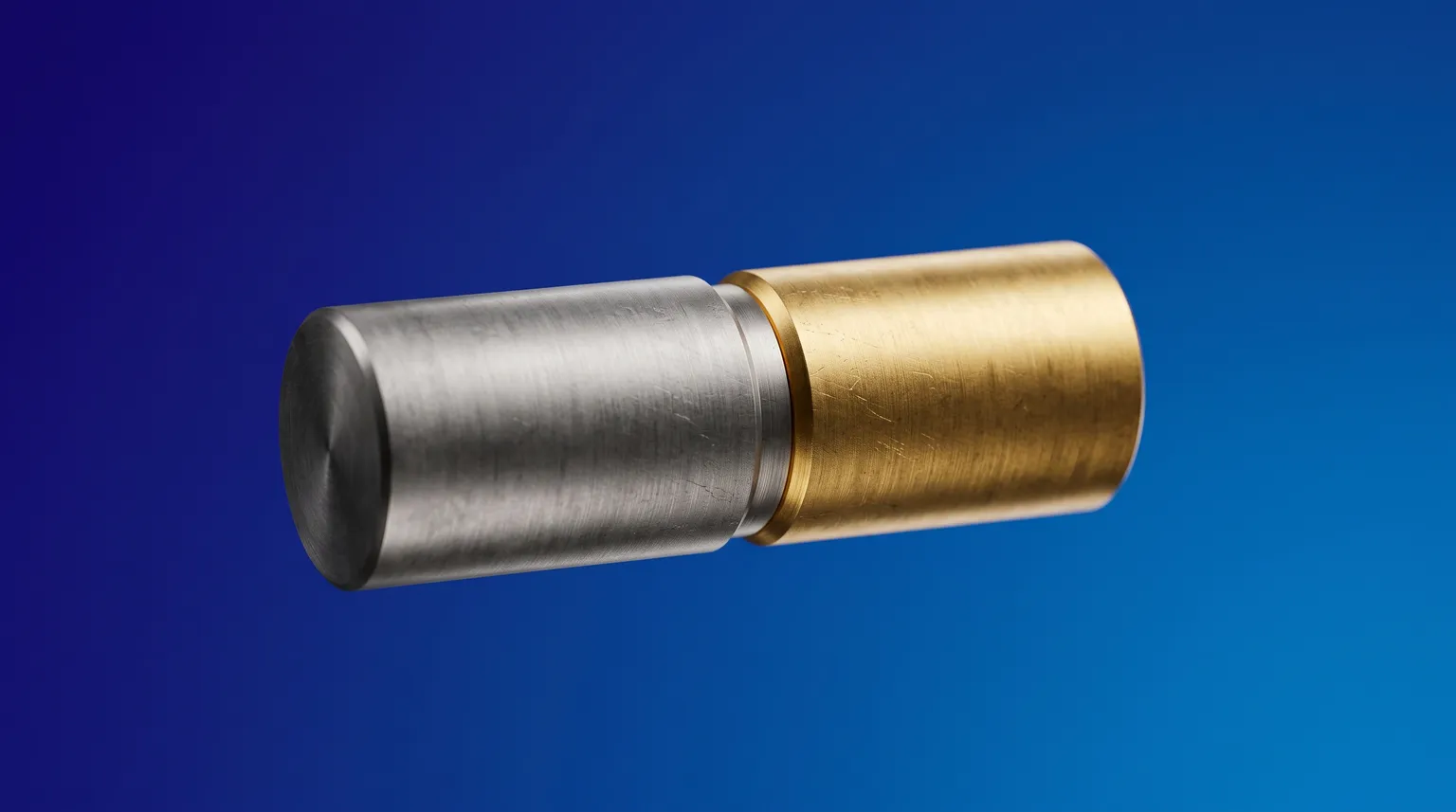 A brushed-steel cylinder and a brass cylinder joined end to end, a gold ring at the join, on deep blue.