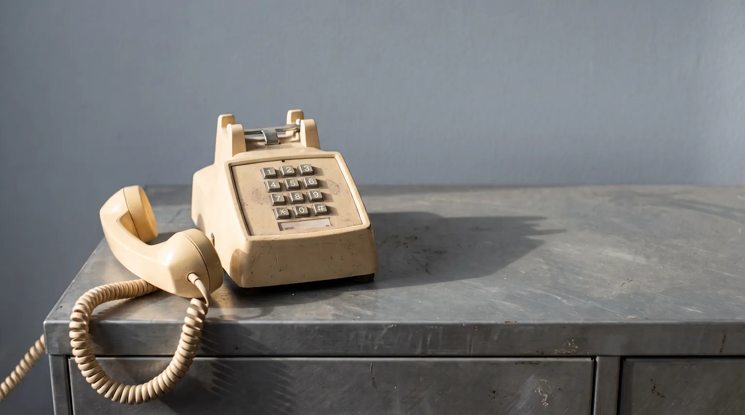 A corded desk phone off the hook on a grey filing cabinet, handset resting beside it.